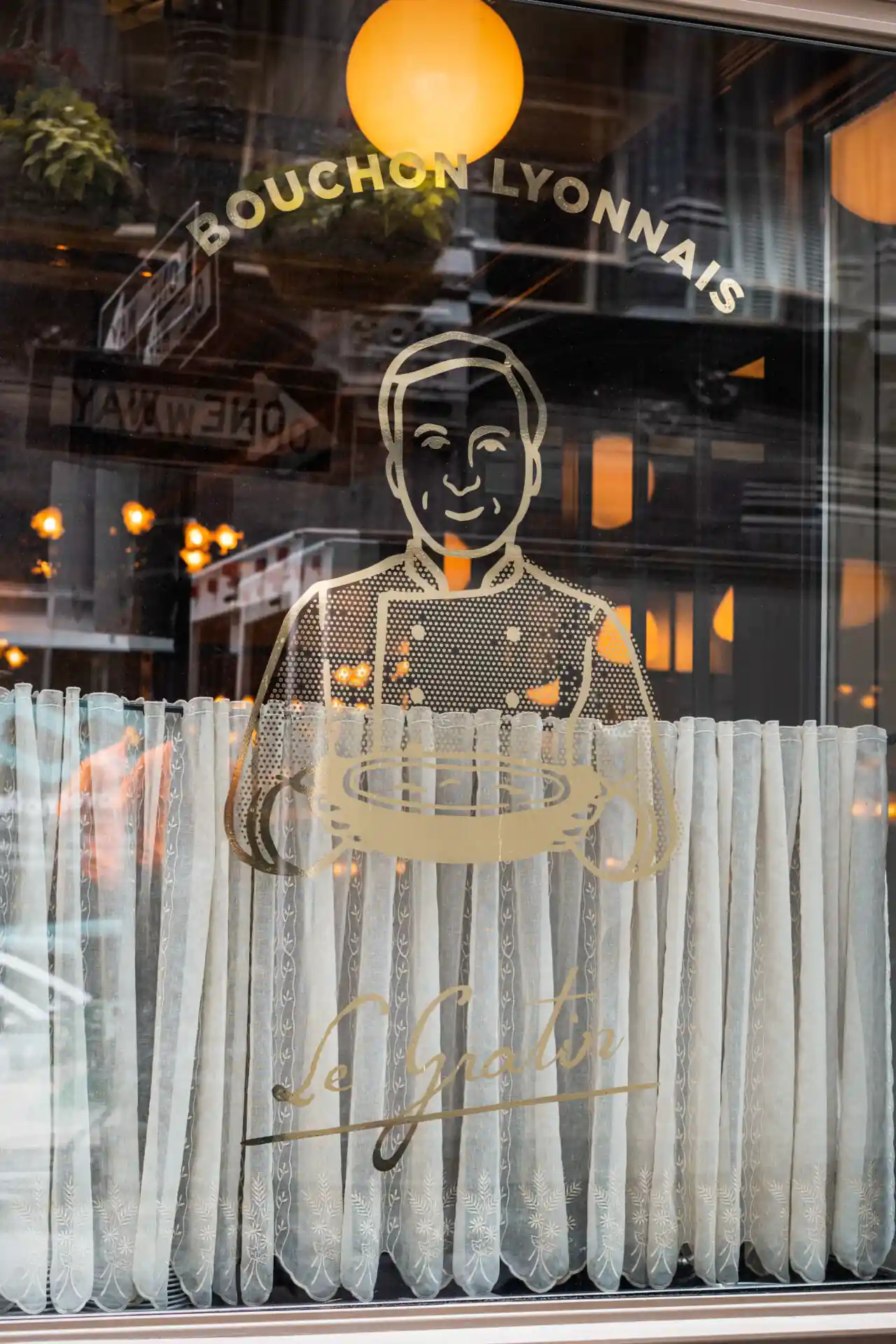 Le Gratin window showcases a chef holding plates in their logo display.