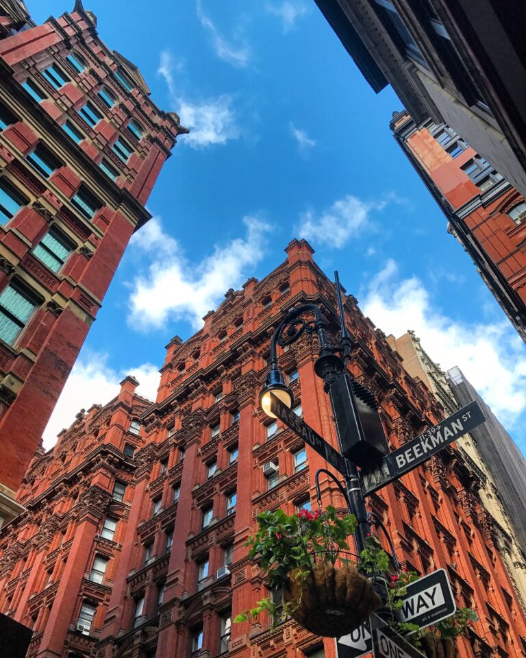 Tall red-brick historic buildings on Beekman Street under bright blue sky with street signs visible.