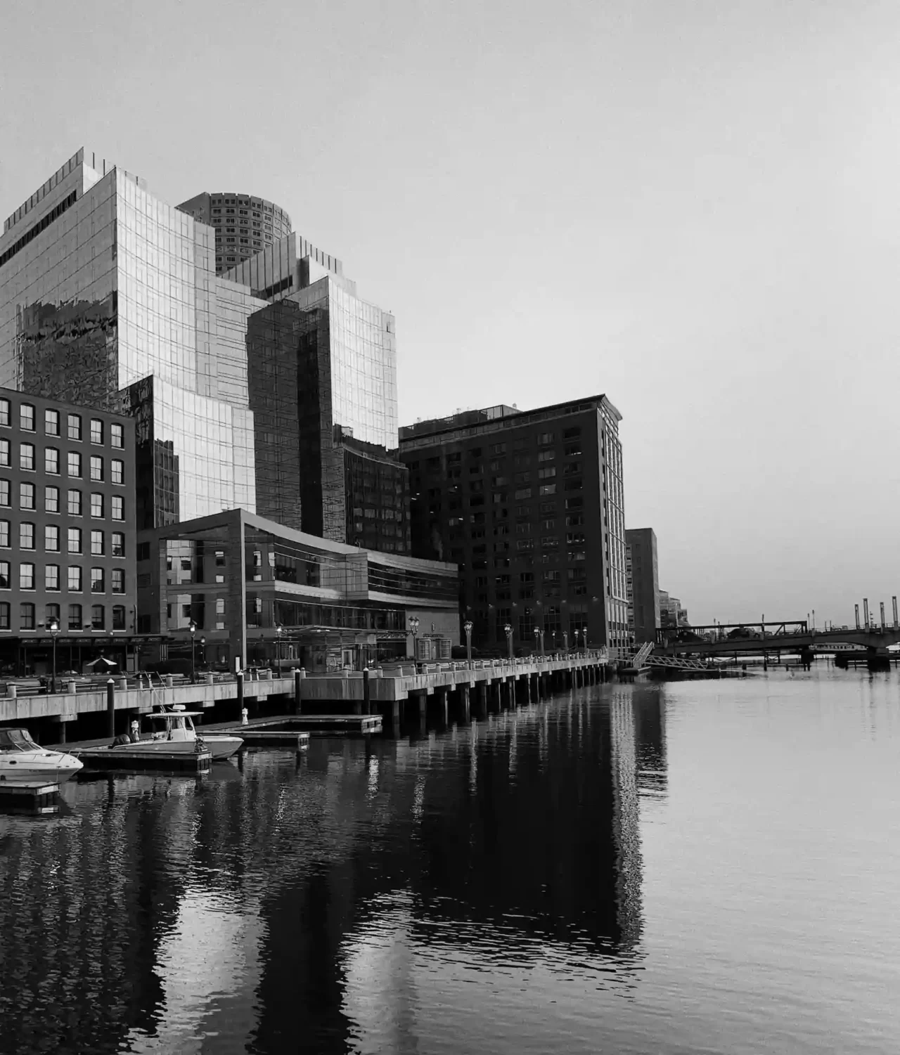 Monochrome photo of a towering building adjacent to a river dock.