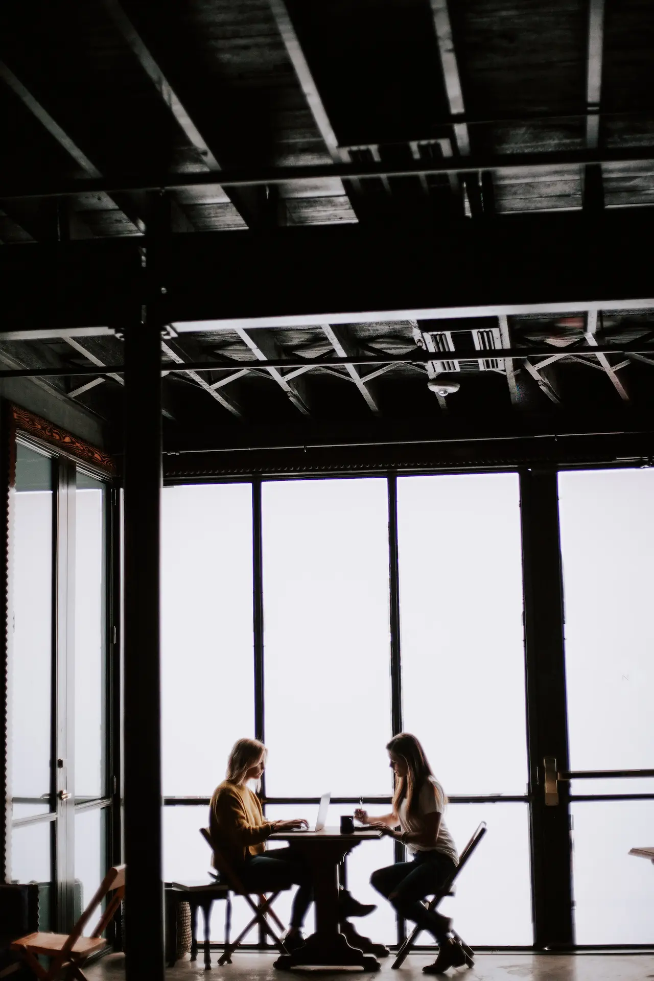 Two girls doing some work at the table just beside the long glass window.